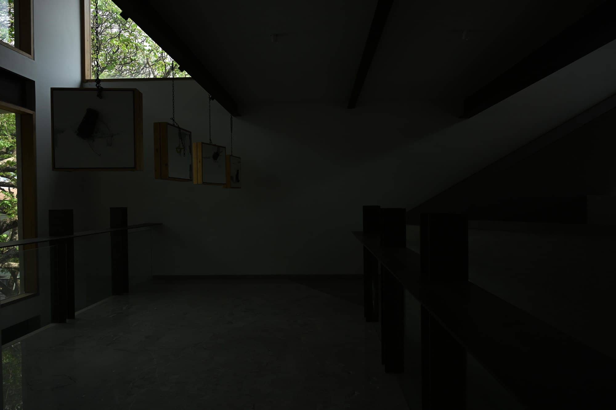 Sloped-ceiling gallery landing with framed works and railing — after dark