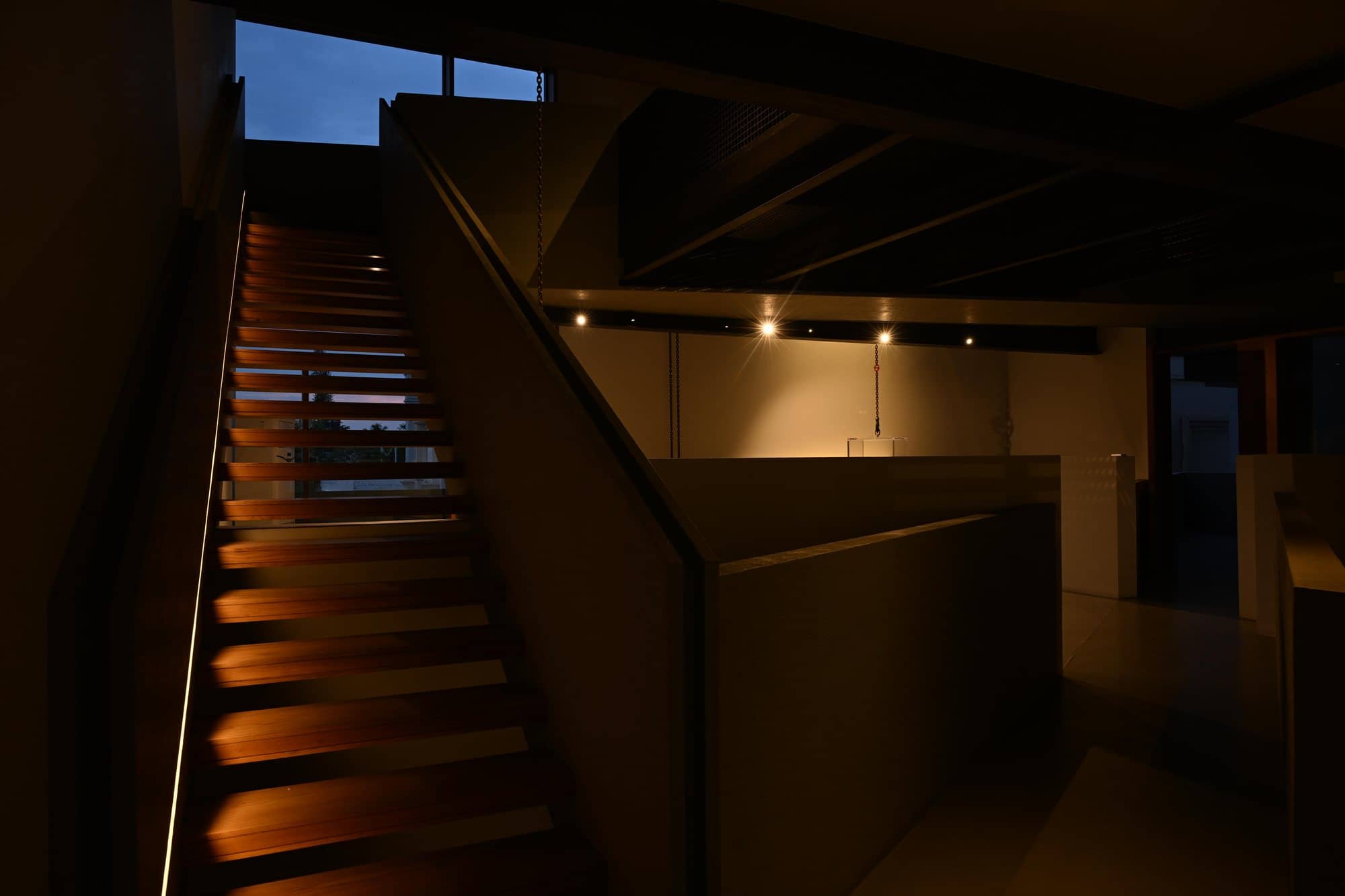 Warm timber-slat staircase rising through the volume — after dark