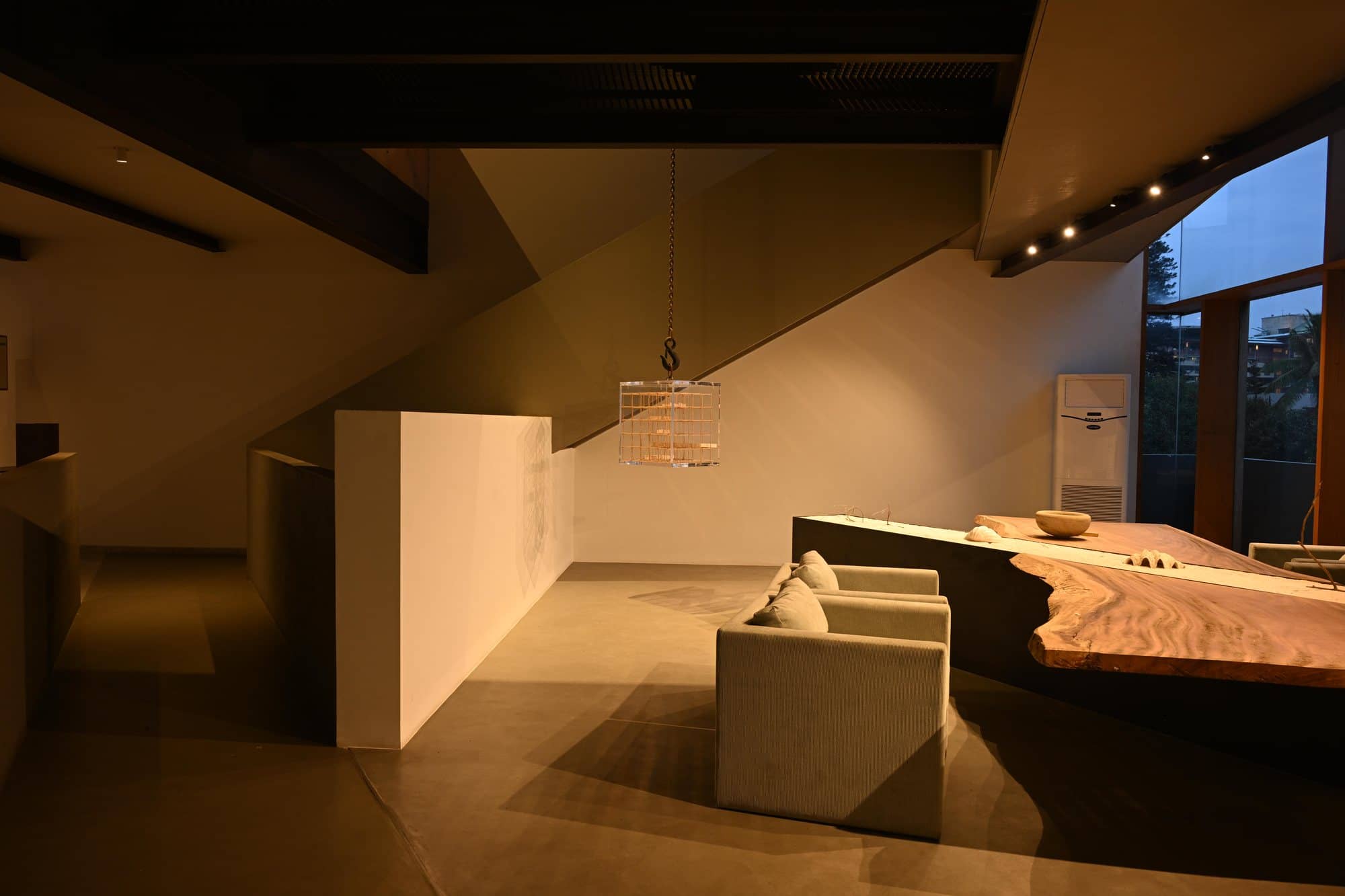 Sculptural wood worktable beneath the sloped roof — after dark