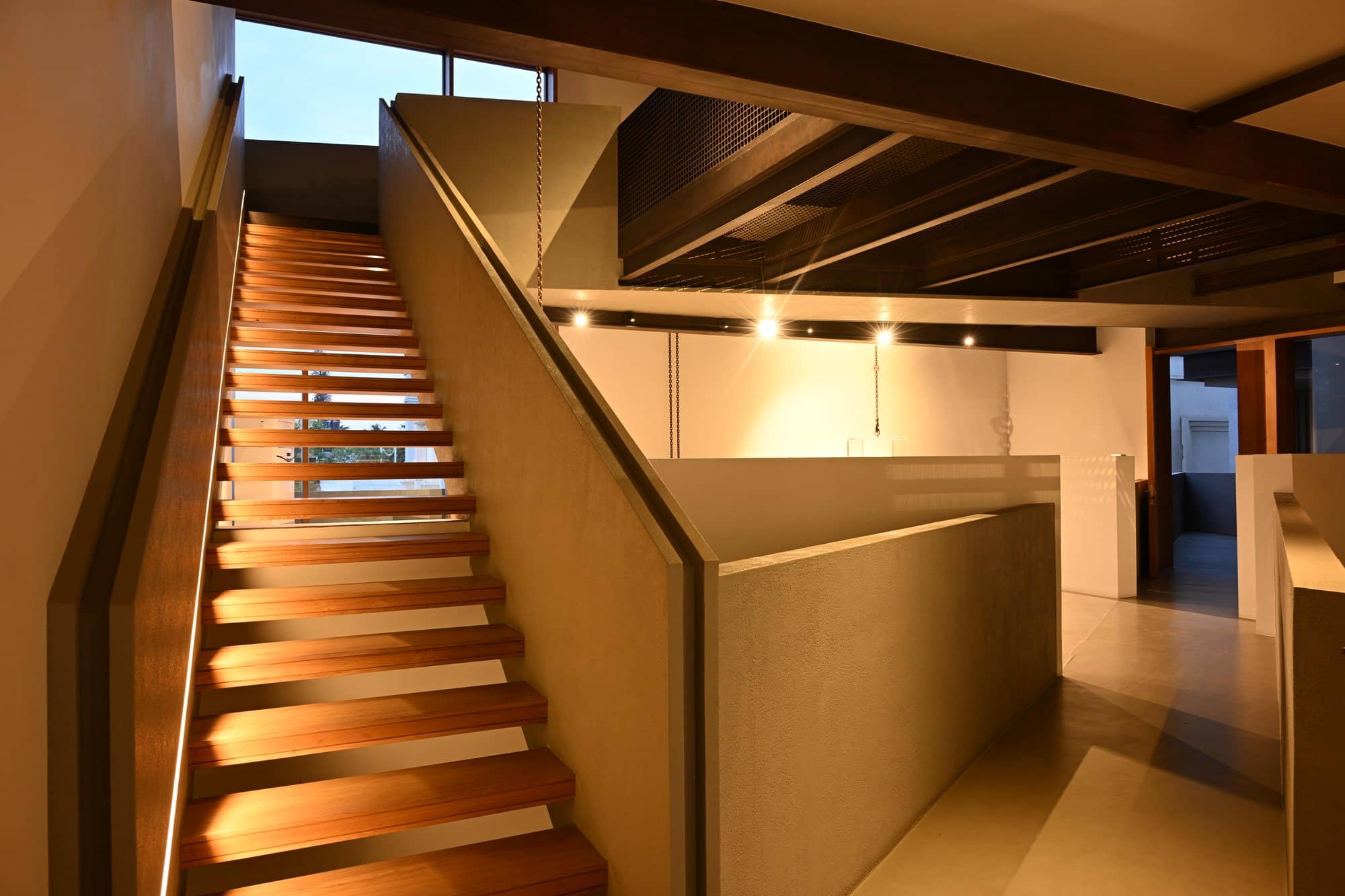 Warm timber-slat staircase rising through the volume — daylight